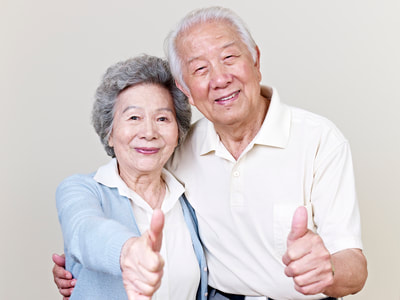 An  old asian couple are holding up their thumbs and smiling.