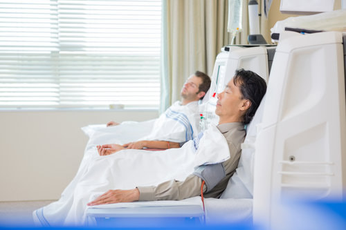 Two males in a hospital room doing their dialysis treatment.