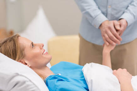 Patient laying in bed holding a mans hand.