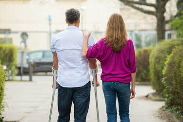 Female walking with male on crutches.