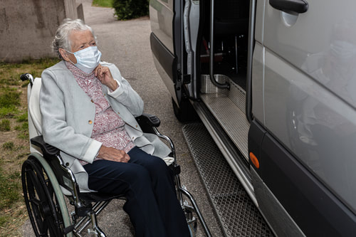 Older lady sitting in a wheelchair next to a van.