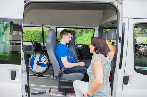 Handicap male sitting in a van being accompanied by a female.